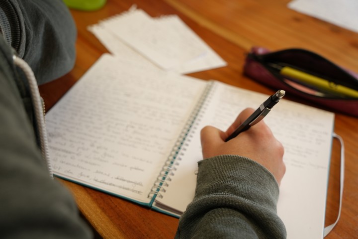Personne en train d'écrire son récit de vie sur un cahier. Le stylo à la main, elle réfléchit à la suite de son texte